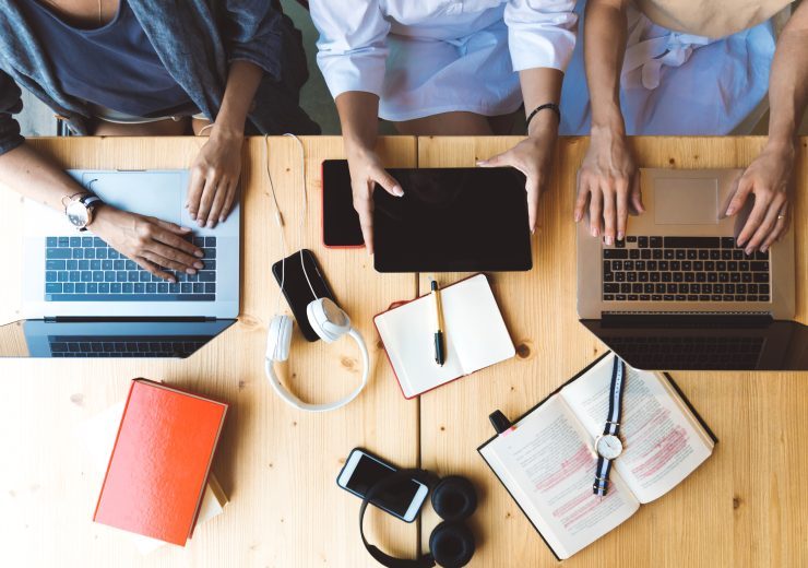 Flat lay picture of three women working with laptops and books sitting at the table together - business woman, co-working and college girls studying concept